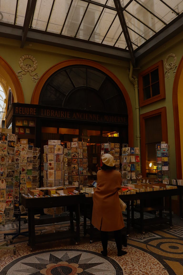 A cozy Parisian bookstore filled with books and postcards, featuring a person browsing inside a picturesque passageway.